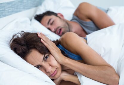 A woman laying in bed next to a man who is sleeping.