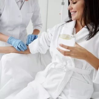 A woman in white robe holding wine glass while another person is wearing gloves.